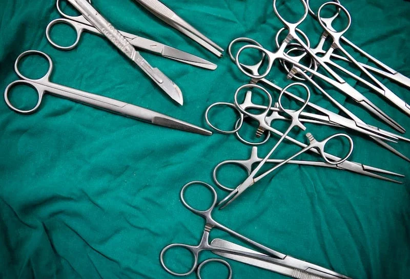 Sterile surgical instruments including scissors, clamps, and scalpel laid out on a green operating room drape