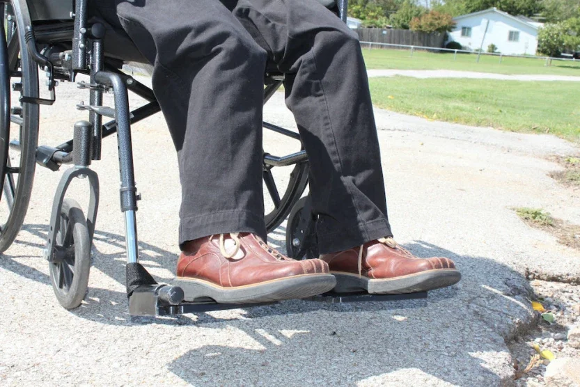 Person in a wheelchair outdoors showing legs and brown shoes resting on footrests