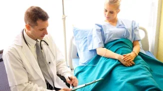 Doctor with stethoscope reviewing patient chart beside woman in hospital bed with IV line