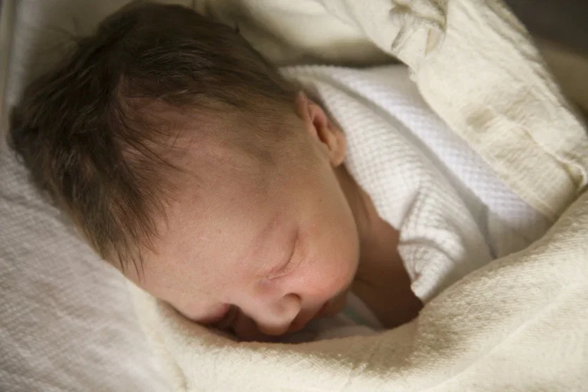 Newborn infant sleeping peacefully swaddled in white hospital blanket shortly after birth