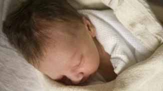 Newborn infant sleeping peacefully swaddled in white hospital blanket shortly after birth