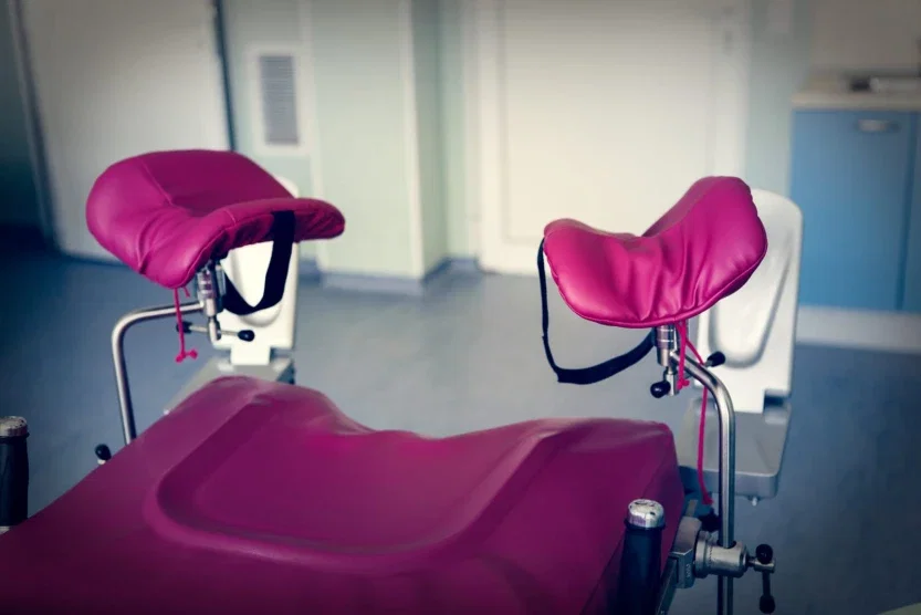 Close-up of pink padded stirrups on a gynecological exam table in a medical clinic