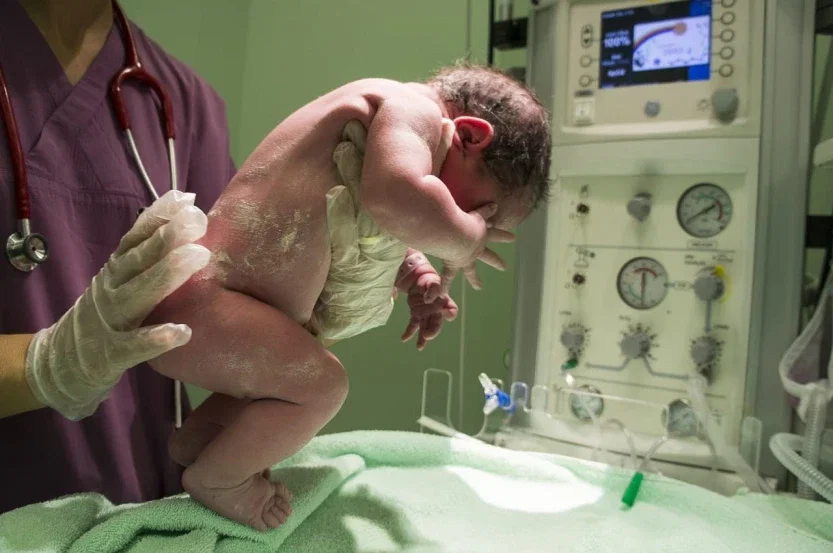 Medical professional in gloves holding a newborn seconds after delivery in a hospital birthing room