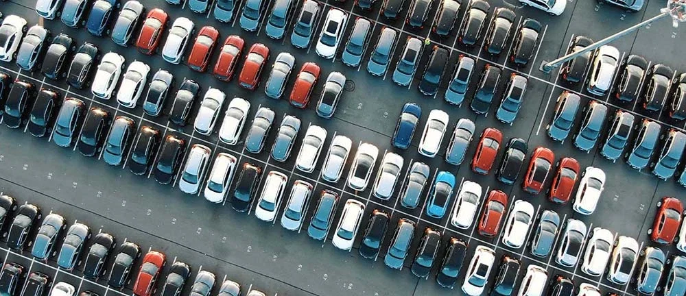 Aerial top-down view of rows of new vehicles in various colors parked in a large automotive lot or distribution facility