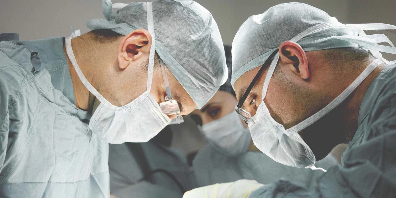 Two surgeons in masks and caps working closely together during an operation representing surgical malpractice claims