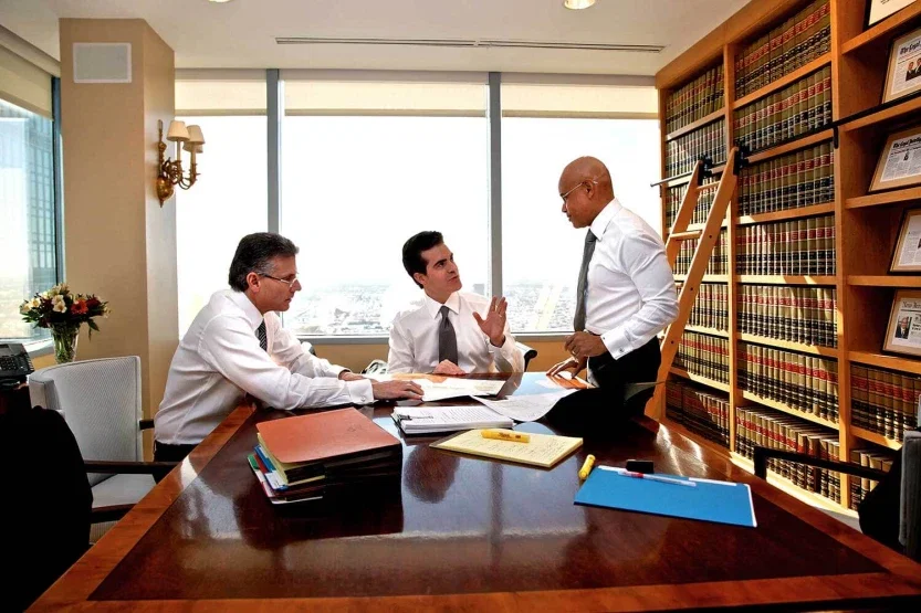 Three personal injury attorneys reviewing case documents at desk in law library office setting
