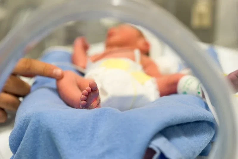 Premature newborn lying in NICU incubator receiving care after complicated birth injury