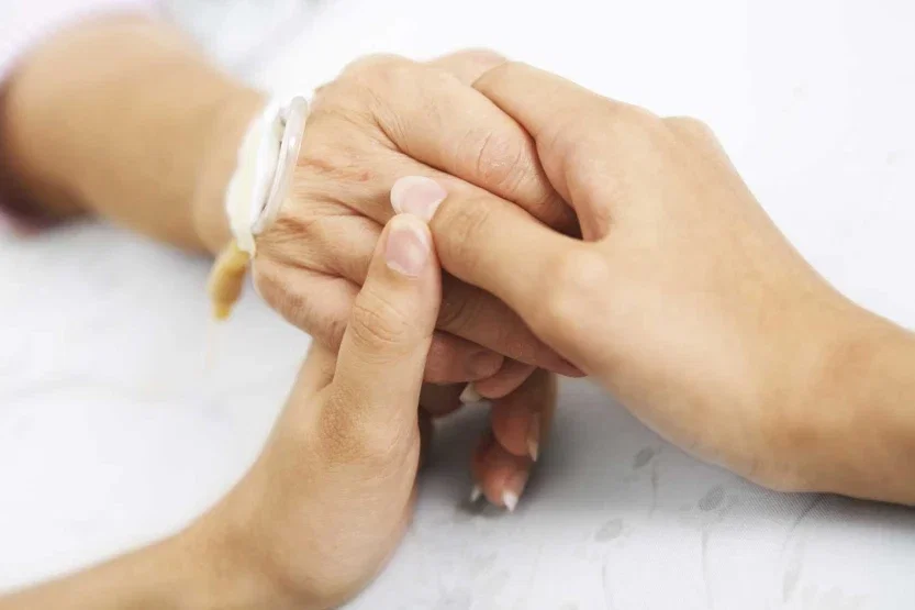 Family member holding elderly hospital patient hand with ID bracelet representing wrongful death injury claim