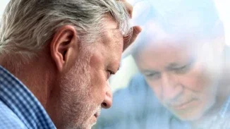 Distressed older man resting head against window reflecting on serious medical malpractice injury