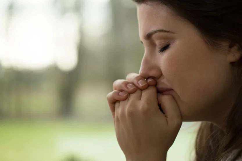 Young woman with eyes closed and hands clasped coping with trauma after personal injury