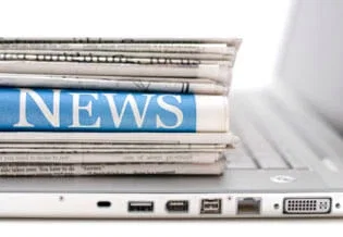 Stack of newspapers with NEWS headline resting on laptop keyboard representing online and print legal media coverage