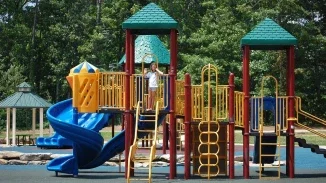 Child waving from colorful playground structure with spiral slide representing premises liability and playground injury claims