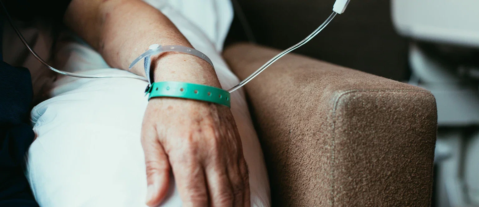 Elderly hospital patient with IV line and identification bracelet resting after surgery or medical treatment