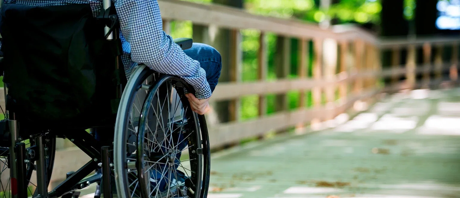Person in a wheelchair moving along an outdoor wooden path representing spinal cord injury and paralysis claims