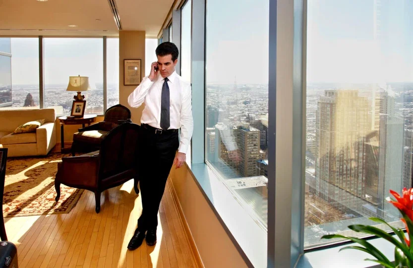 Personal injury attorney on phone call beside floor-to-ceiling windows with sweeping city skyline view from high-rise office