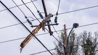 A damaged wooden utility pole crossarm, split and leaning at an angle, with power lines and insulators tangled against an overcast sky