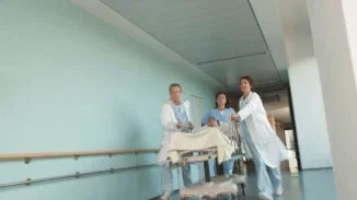 A motion-blurred image of three medical staff members in white coats and scrubs rushing a patient on a gurney down a hospital corridor