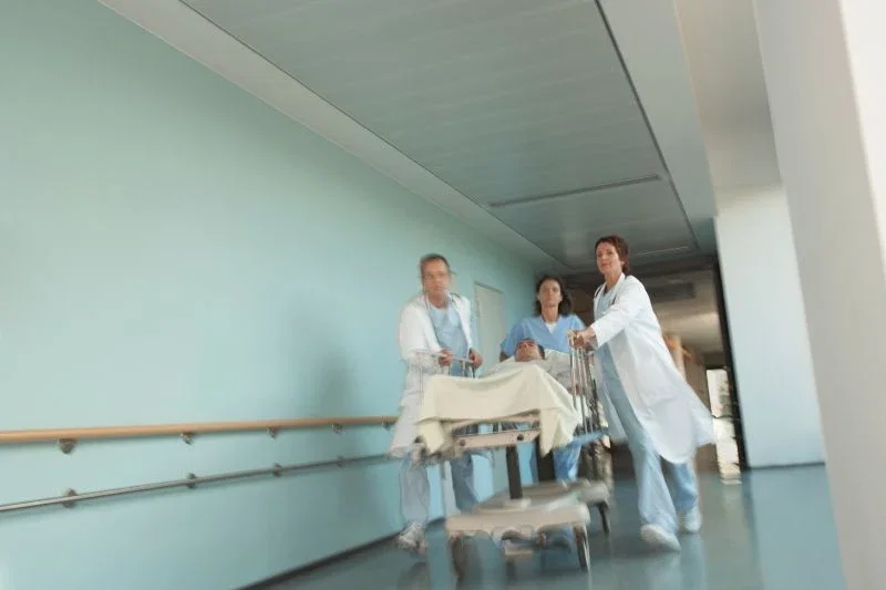 A motion-blurred image of three medical staff members in white coats and scrubs rushing a patient on a gurney down a hospital corridor