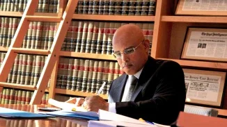 Personal injury attorney writing notes on legal documents at desk surrounded by floor-to-ceiling law library shelves