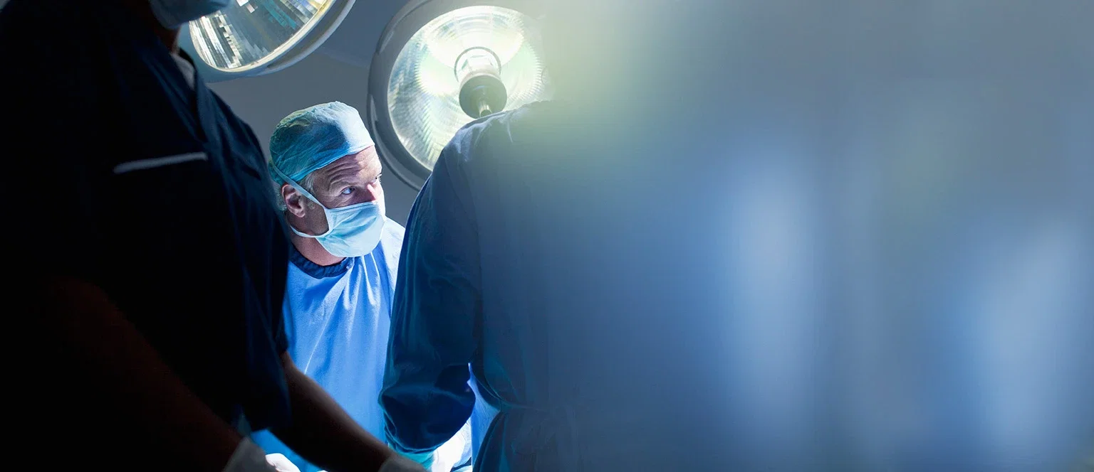 Surgeon in surgical cap and mask under bright operating room lights during a medical malpractice case