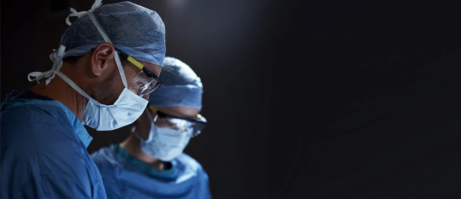 Surgical team in masks caps and safety glasses focused during an operation in a darkened operating room