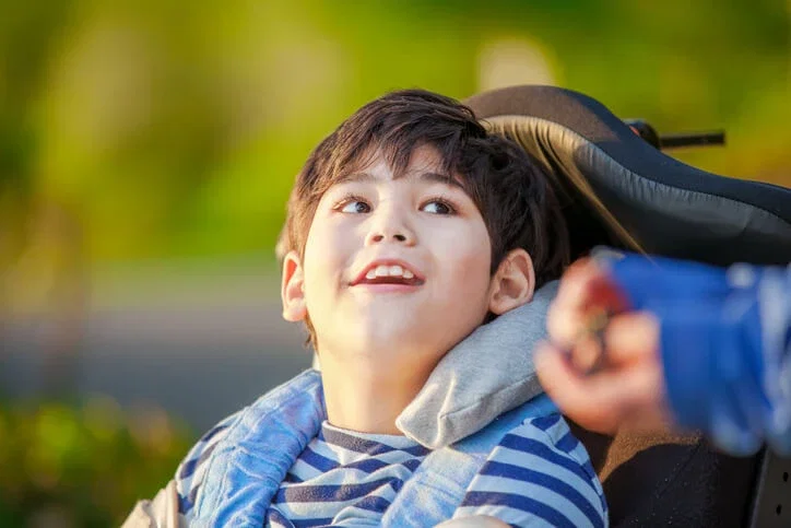 Smiling child in adaptive wheelchair outdoors representing catastrophic injury and birth injury legal cases